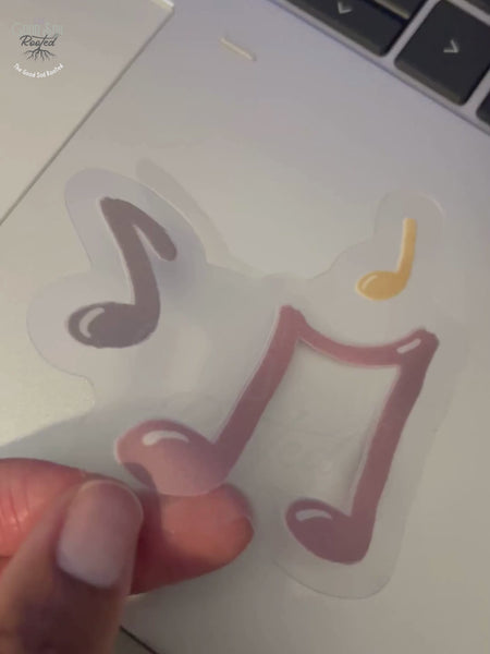 Hand placing a clear vinyl sticker designed with pink, purple and yellow music notes.