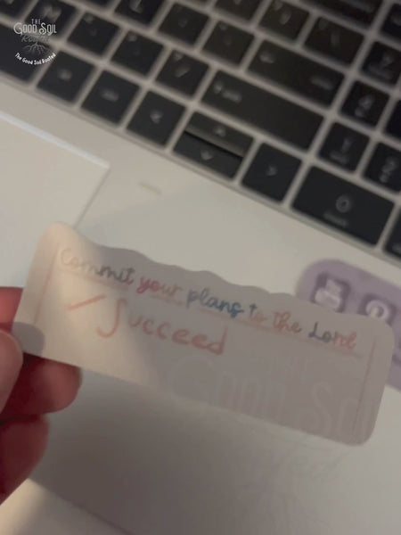 Video clip of Sticker with text that states commit your plans and a checked box that says succeed, being placed on laptop for decoration.